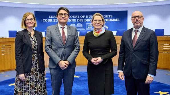 Stefanie Hubig with a colourful scarf, standing with three colleagues in the courtroom of the European Court of Human Rights in Strasbourg.