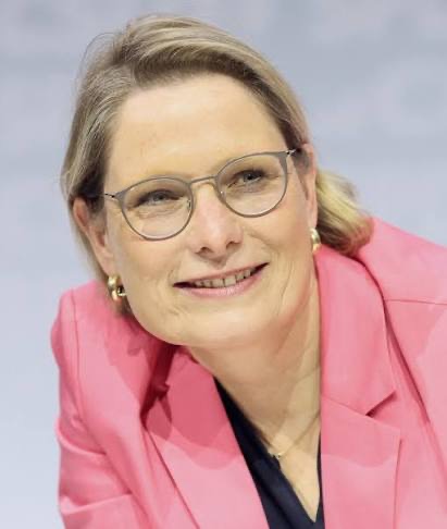 Portrait of Stefanie Hubig smiling, in a pink blazer and glasses.