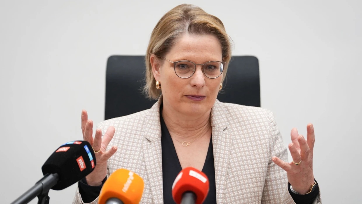 Stefanie Hubig seated behind several broadcasters’ microphones, gesturing with both hands while giving a press statement.