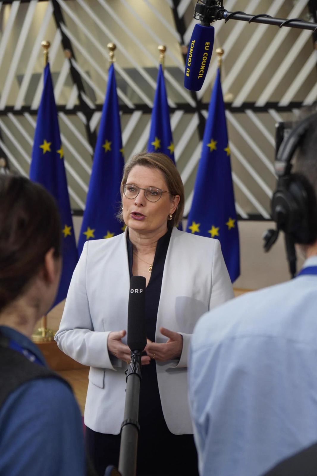 Stefanie Hubig speaking to journalists’ microphones in front of a row of European Union flags at the Council of the EU in Brussels.