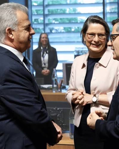 Stefanie Hubig in a pale pink jacket smiling as she talks with two male colleagues at a meeting table of the Council of the EU.