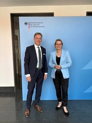 Stefanie Hubig in a light-blue blazer standing beside a man in a dark suit in front of a Federal Ministry of Justice and Consumer Protection backdrop.