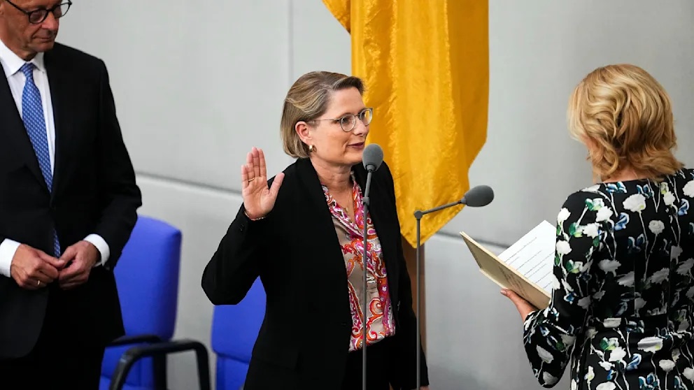 Stefanie Hubig raising her right hand to take the oath of office in the Bundestag, facing the President of the Bundestag, with a federal flag behind her.