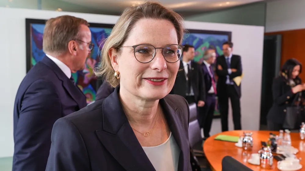 Stefanie Hubig smiling in the federal cabinet room, with a round conference table and other cabinet members in the background.
