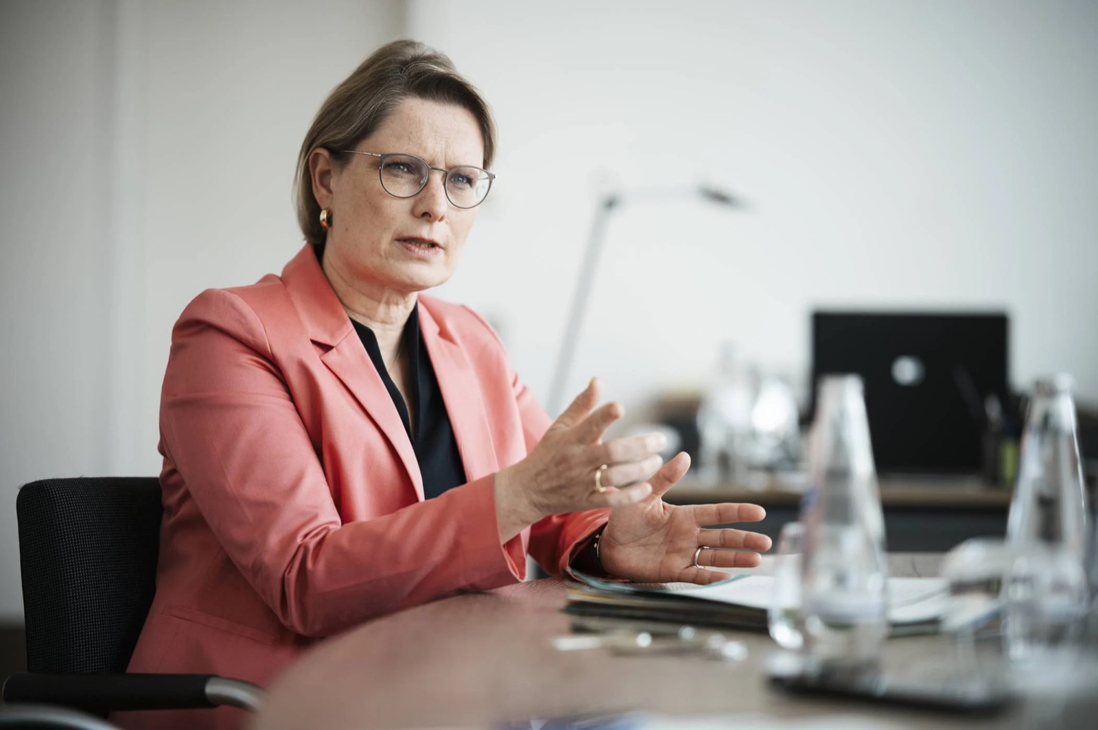 Stefanie Hubig in a coral blazer seated at a conference table, gesturing while speaking during an interview.