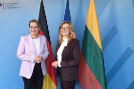 Stefanie Hubig in a pale pink blazer standing beside a woman in a dark blazer in front of German, EU and Lithuanian flags.