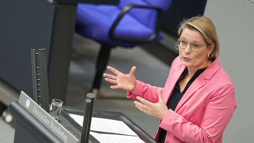Stefanie Hubig in a pink blazer speaking from the Bundestag lectern, gesturing with both hands; the lectern sign reads Deutscher Bundestag.