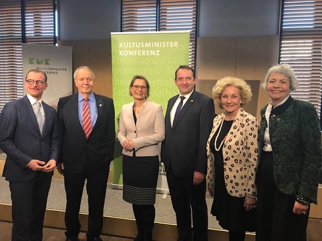Group of six people, including Stefanie Hubig in a pale blazer, standing in front of a green banner of the Standing Conference of the Ministers of Education and Cultural Affairs (Kultusministerkonferenz).